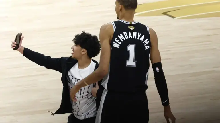 A fan runs onto the court and takes a photo with Victor Wembanyama #1 of the San Antonio Spurs during the fourth quarter in Game One of the 2026 NBA Finals against the New York Knicks at Frost Bank Center on June 03, 2026 in San Antonio, Texas.
