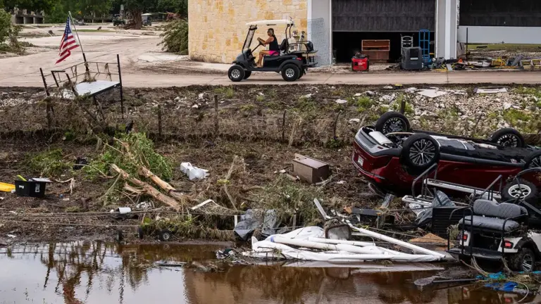 A woman drives past vehicles and golf carts washed out of Buckhorn Lake Resort and onto the shoulder of the Interstate 10 frontage road near Goat Creek Road by flooding, July 17, 2026.