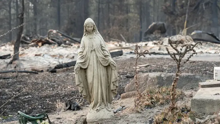 A Virgin Mary statue remains untouched in front of a burned out residential home in the Balboa neighborhood of Spokane, Washington, on August 2, 2026. Fast-moving fires left a trail of destruction in the northwestern US city of Spokane on Sunday, with officials reporting hundreds of structures reduced to cinders.